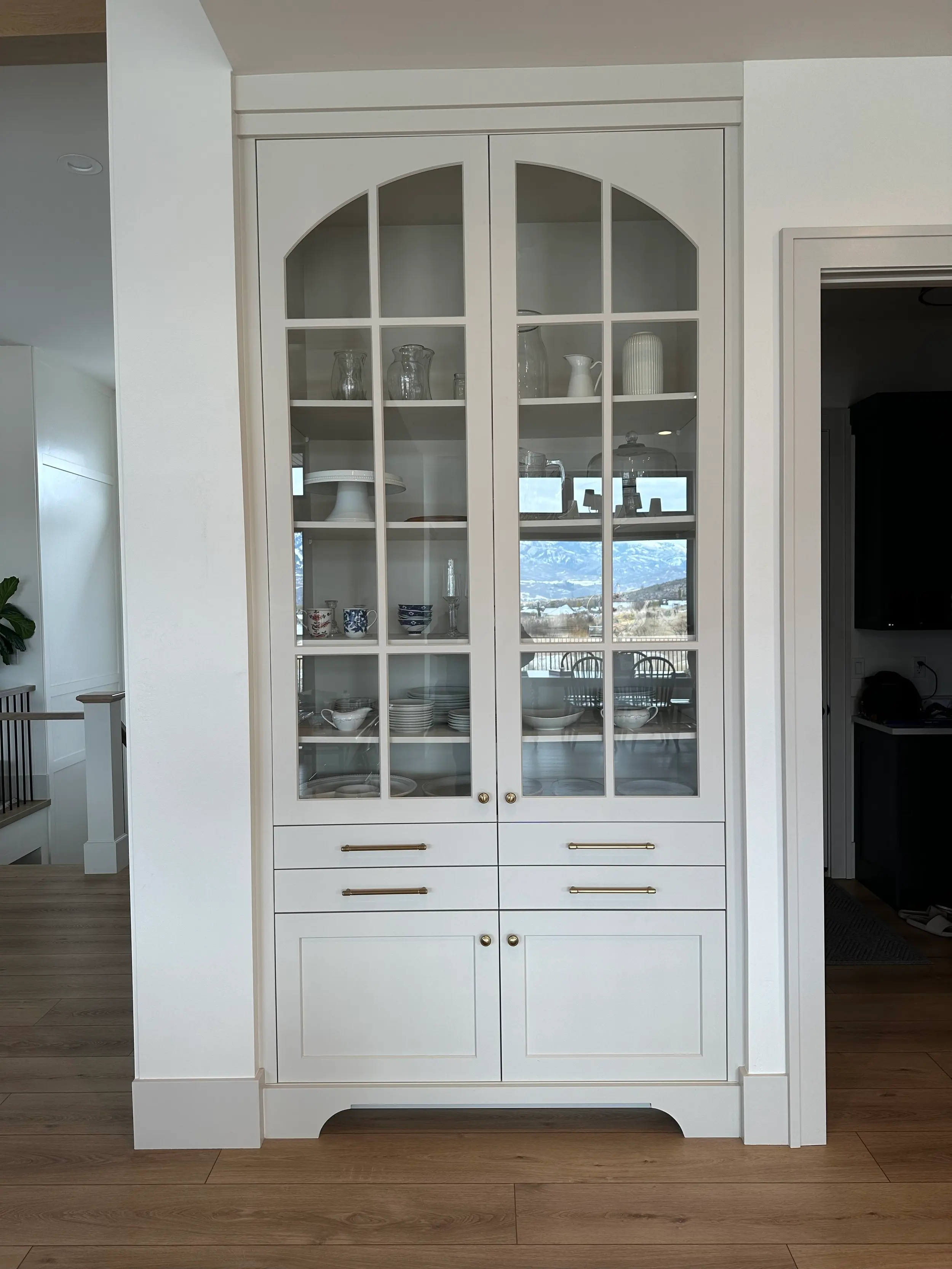 Custom built-in hutch cabinet with arched glass-front doors, brass hardware, and lower drawer and door storage for dinnerware display.